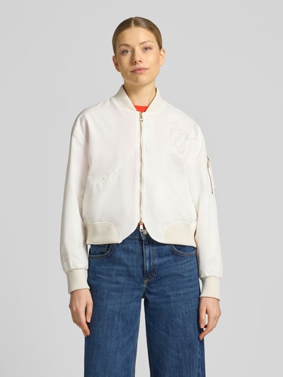 Modelka kobieca nosi Bomberjacke mit Zweiwege-Reißverschluss od Original Bombers, kremowy kolor, krój regular fit, stebnowanie, stehnij kołnierz, dwukierunkowy zamek, kieszenie na zamek, długość tyłu w rozmiarze S: 55 cm, szerokość ramion w rozmiarze S: 50 cm, szerokość klatki piersiowej w rozmiarze S: 56 cm, długość rękawa w rozmiarze S: 64 cm, jeansowe spodnie, gładka tekstura, widok całej sylwetki z przodu.