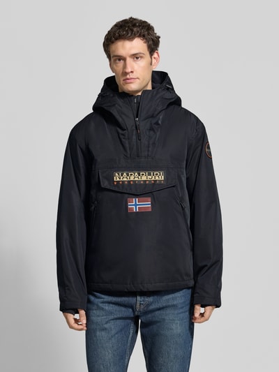 Männermodel trägt Jacke mit Kapuze und kurzem ritssluiting van Napapijri, recht model, Klepzak, labelpatches, kleur zwart, Ganzkörperansicht van voren. Ruglengte maat M 73 cm, schouderbreedte 53 cm, borstwijdte 60 cm, mouwlengte 64 cm.