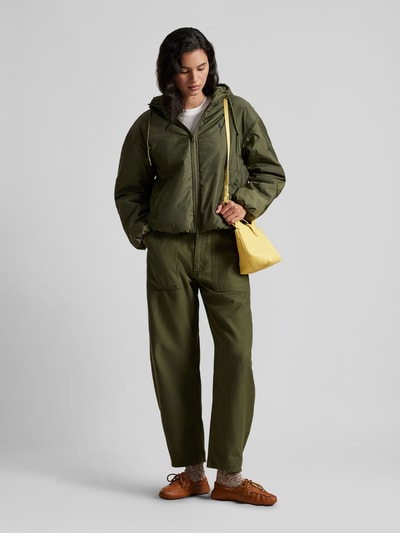 Modelka nosi Relaxed Fit Blouson mit Zweiwege-Reißverschluss od Polo Ralph Lauren, zielony kolor, jednolita faktura, długość do bioder, z kapturem, krój relaxed fit, naszywane logo, balonowe rękawy i elastyczne wykończenia; widok całej sylwetki z przodu.