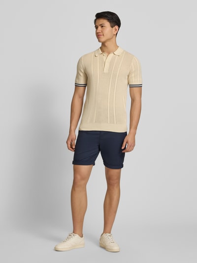 Męski model nosi Regular Fit Shorts mit Münztasche von Superdry, granatowe, mieszanka bawełny, kieszonka na monety, z tyłu kieszeń, zapięcie na guzik i zamek błyskawiczny, szerokość w rozmiarze 32: 44 cm, długość wewnętrzna nogawki w rozmiarze 32: 20 cm, krój regular fit, całkowity widok z przodu.