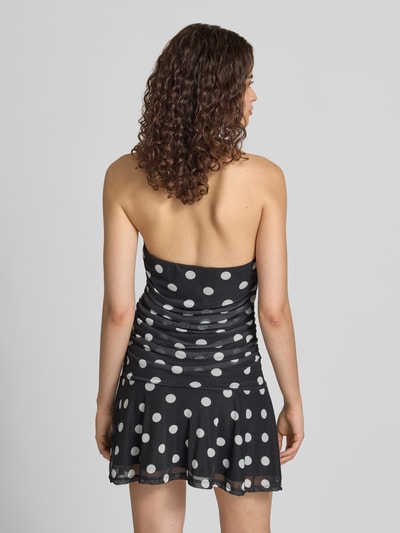 Frauenmodel trägt Neckholder-Minikleid im Allover-Look Modell 'DOTTIE' von NOISY MAY®, schwarzer Stoff mit weißen Punkten, Material-Mix mit Stretch-Anteil, Rückenansicht Ganzkörperansicht.