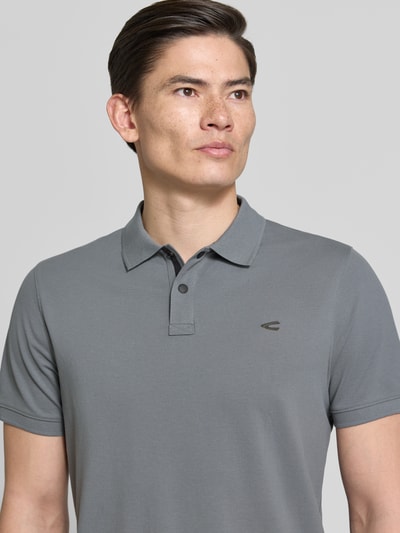 Mannmodel draagt Regular Fit Poloshirt in unifarbenem Design van camel active, katoen-elastaan mix, grijs, logo, knoopsluiting, bovenlichaam close-up.