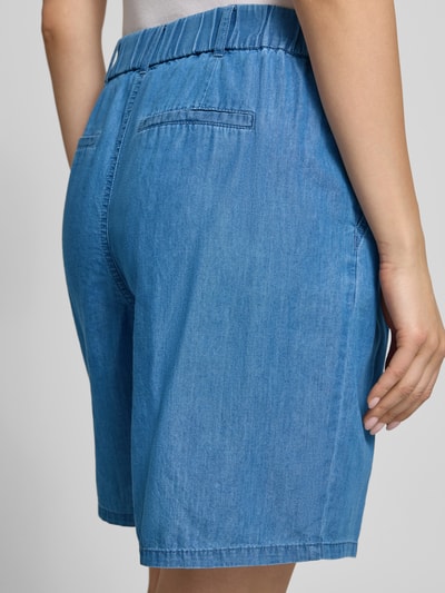 Kobiece modelka ma na sobie szorty jeansowe Relaxed Fit Jeansshorts aus Baumwoll-Lyocell-Mix Modell 'BEA' od Only, kolor niebieski, tkanina stylizowana na denim, z zakładką w pasie, elastycznym pasem, wpuszczane kieszenie boczne, mieszanka bawełny i lyocellu, ujęcie detaliczne tyłu.