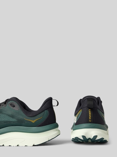 Produktfoto, Sneaker mit Label-Details und Schnürverschluss von HOKA, Textil in Dunkelgrün und Schwarz, profilierte Sohle, abgerundete Form, Absatzhöhe 6 cm, Schafthöhe 7 cm, Schaftweite 6 cm, Label seitlich und Ferse, neutrale Hintergrundfarbe.