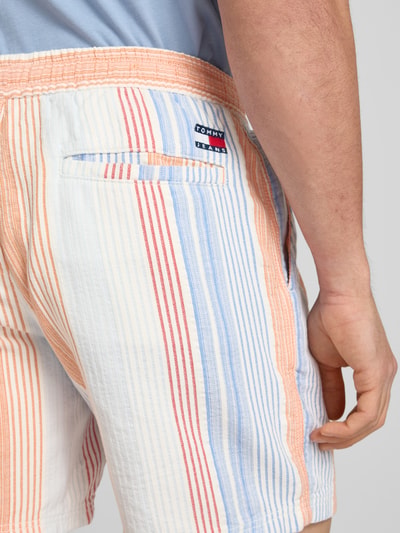 Männermodel trägt Relaxed Fit Shorts aus reiner katoen van Tommy Jeans met all-over motief look, labelpatch, boord met tunnelkoord, zij-steekzakken, dobby materiaalverwerking, pastelroze, lichtblauwe en witte verticale strepen, detailopname rug.