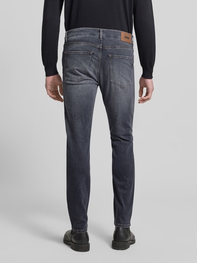 Männermodel trägt Slim Fit Jeans aus Baumwoll-Mix Modell 'DELAWARE' von BOSS in grauer Denim-Optik mit Label-Patch, Ganzkörperansicht Rückansicht.