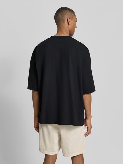 Männermodel trägt schwarzes Herren T-Shirt mit Logo-Print Modell 'GIXY' von American Vintage aus Reine Baumwolle, Loose-Fit, Rückenlänge 72 cm, Ganzkörperansicht Rückansicht.
