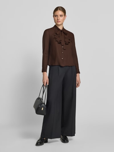Frauenmodel trägt Regular Fit Schluppenbluse mit Rüschen von Christian Berg Woman Selection, braun, schwarze Hose, glatte Textur, Ganzkörperansicht von vorne. Rückenlänge 57 cm, Ärmellänge 60 cm, Knopfleiste.