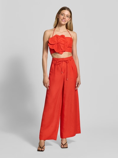 Vrouwenmodel draagt rode set bestaande uit top met strikdetail en wijde broek, gladde linnenmix, eenvoudige achtergrond, volledige voorkant.
