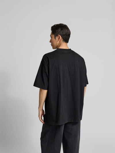 Männermodel trägt Oversized T-Shirt aus Baumwolle von VETEMENTS in Schwarz mit Label-Stitching, Rückenlänge 80 cm, Ganzkörperansicht Rückansicht.