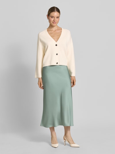 Frauenmodel trägt Strickjacke aus Viskose-Mix mit V-Ausschnitt von comma, cremefarben, Relaxed Fit, Knopfleiste, Ganzkörperansicht von vorne.