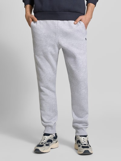 Männermodel trägt Slim Fit Sweatpants mit Logo-Stitching von REVIEW aus Baumwoll-Mix in Hellgrau, elastischer Bund, Gesäßtasche, Ganzkörperansicht von vorne.