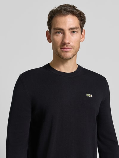 Männermodel trägt schwarzen Regular Fit Pullover aus Baumwoll-Mix von Lacoste, dezentes Lacoste-Logo, Nahaufnahme Oberkörper.
