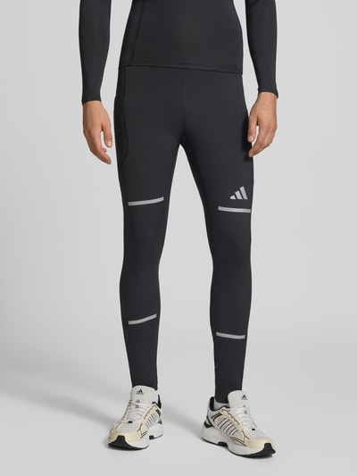 Männermodel trägt schwarze Slim Fit Trainingshose mit reflektierenden Details Modell 'adi' von adidas Training, Nahaufnahme Unterkörper.