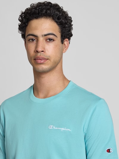 Männermodel trägt T-Shirt mit Logo-Stitchings Modell 'ICONS CONTRAST' von CHAMPION in Hellblau, Baumwoll-Mix, Modern Fit, Nahaufnahme Oberkörper.