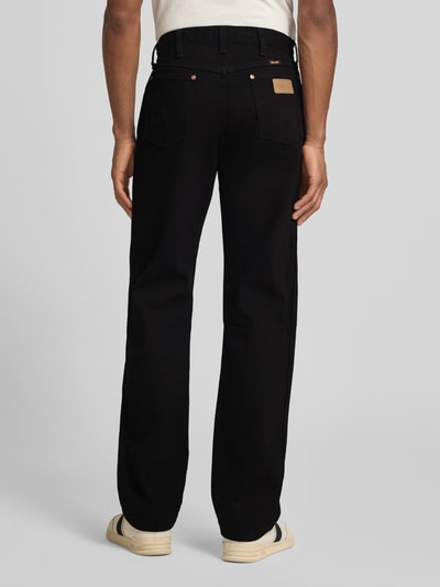Männermodel trägt schwarze Cowboy Cut Jeans im 5-Pocket-Design von Wrangler aus reiner Baumwolle, gerader Schnitt, Ganzkörperansicht Rückansicht.