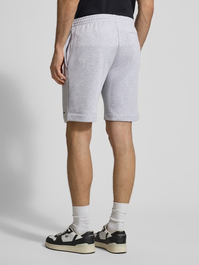 Mężczyzna nosi Regular Fit Sweatshorts aus Baumwoll-Mix od Lacoste, jasnoszary, jednolity, kieszenie boczne, detal logo, krój regular fit, widok całej sylwetki z tyłu.
