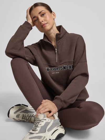 Frauenmodel trägt Sweatshirt mit Stehkragen und Reißverschluss von aim'n im Baumwoll-Mix, Relaxed Fit, Label-Print, Ganzkörperansicht von vorne.