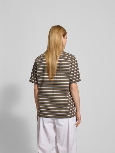 Frauenmodel trägt Oversized T-Shirt mit Logo-Patch von ROTATE aus reiner Baumwolle, gestreiftes Kurzärmeliges Design, Rückenlänge 70 cm, Ganzkörperansicht Rückansicht.