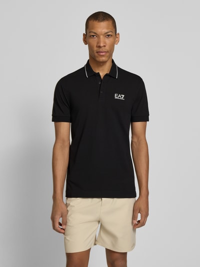 Männermodel trägt Regular Fit Poloshirt mit Logo-Print von EA7 Emporio Armani in Schwarz, Kurzarm, Polokragen, Vorderansicht Ganzkörperansicht.