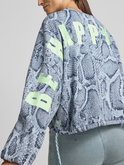 Frauenmodel trägt Oversized Sweatshirt aus Baumwoll-Mix von Marc Cain mit Schlangenprint, Ballonärmel und Schriftzug, Nahaufnahme Rückansicht.