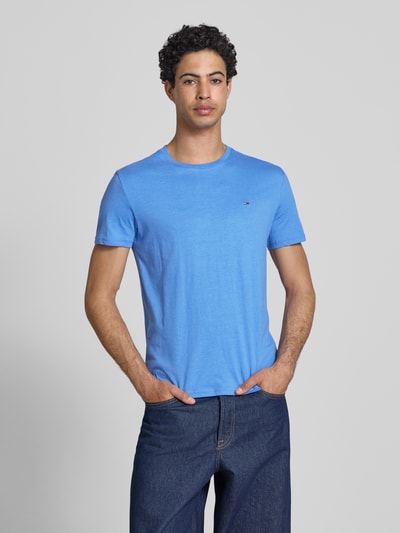 Mężczyznęmodel nosi niebieski Slim Fit T-Shirt Modell 'TJM XSLIM JASPE HTR TEE E' od Tommy Jeans, jednolity kolor, logo haftowane, dekolt w serek, krótki rękaw, krój slim fit, widok całej sylwetki z przodu.
