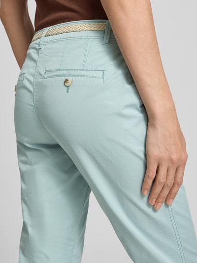Kobiecy model nosi Slim Fit Chino aus Baumwoll-Mix od Tom Tailor, kolor jednolity, krój slim fit, bawełniany materiał, kontrastowe szwy, kieszenie boczne i tylne, pasek, dół nogawki z mankietem, zapięcie na guzik i kryty zamek, zbliżenie na tył.