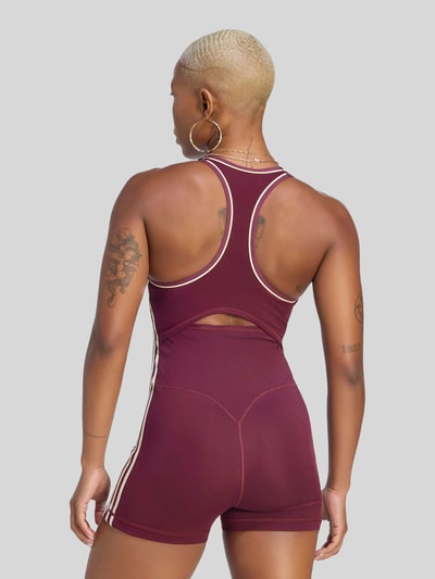 Frauenmodel trägt Slim Fit Sport-Jumpsuit mit Kontraststreifen von adidas, dunkles Rot mit weißen Akzenten, Damen Sport-Jumpsuit von adidas Training, Ganzkörperansicht Rückansicht.