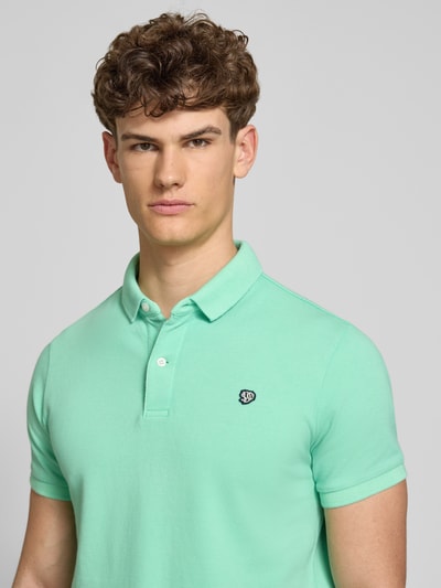 Männermodel trägt Regular Fit Poloshirt mit Logo-Stitching von Superdry in Mintgrün, Reine Baumwolle, Polokragen, Kurzärmelig, Nahaufnahme Oberkörper. Rückenlänge bei Größe M: 67 cm.