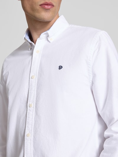 Männermodel trägt Regular Fit Freizeithemd mit Logo-Stitching von Superdry, Reine Baumwolle, Button-Down-Kragen, Knopfleiste, Nahaufnahme Oberkörper.