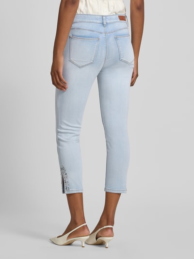 Frauenmodel trägt Slim Fit Jeans mit Viskose-Anteil in verkürzter Passform von Betty Barclay in hellem Blau, 5-Pocket-Design, Ganzkörperansicht Rückansicht, Damen Jeans, elastischer Baumwoll-Mix mit Viskose-Anteil, Knopf- und Reißverschluss, Bundweite bei Größe 36: 35 cm, Innenbeinlänge bei Größe 36: 64 cm.