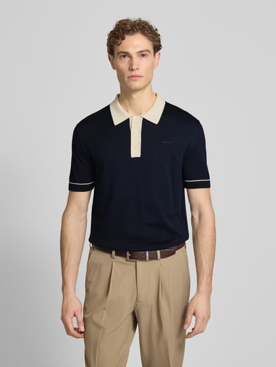 Männermodel trägt Slim Fit Poloshirt mit Logo-Stitching von Gant, dunkelblau mit beigem Kragen, Baumwoll-Modal-Mix, Nahaufnahme Oberkörper.