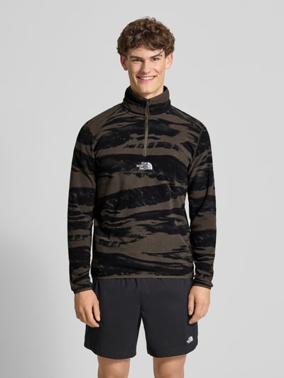 Männermodel trägt Fleecepullover mit Troyer-Kragen von The North Face in Schwarz und Oliv, lockere Passform, Ganzkörperansicht von vorne.
