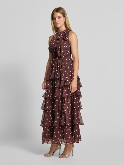 Frauenmodel trägt Abendkleid mit Rüschenbesatz Modell 'Marli' von Neo Noir in Dunkelbraun mit beigen Punkten, taillierter Passform und Zierschleife, Rundhalsausschnitt, ärmelloses Design, Ganzkörperansicht von vorne.