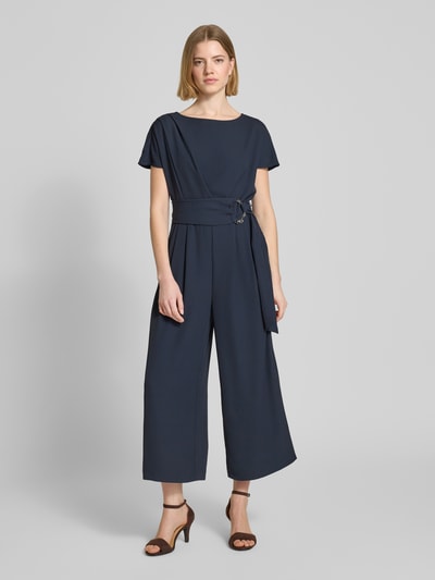 Vrouwenmodel draagt Jumpsuit met Stretch-Anteil van Betty Barclay in donkerblauw elastische materiaalmix, regular fit, ronde hals, riem op taillehoogte, met korte mouwen, 7/8-lengte, plooien, totale lengte 127 cm, ruglengte 38 cm, borstwijdte 37 cm, mouwlengte 23 cm, binnenbeenlengte 58 cm, geheel van voren.