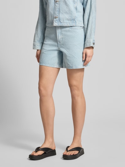 Frauenmodel trägt Jeansshorts im 5-Pocket-Design Modell '90S' von Calvin Klein Jeans aus Reine Baumwolle, Wide-Fit, Label-Detail, Knopf-Reißverschluss, hellblaue Denimstruktur, Ganzkörperansicht von vorne.