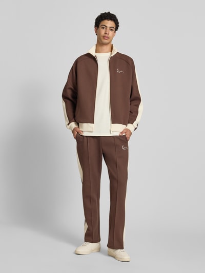 Männermodel trägt Straight Fit Sweatpants mit Logo-Stitching von KARL KANI in Braun mit Ziernähte, Elastischer-Material-Mix, Ganzkörperansicht von vorne.