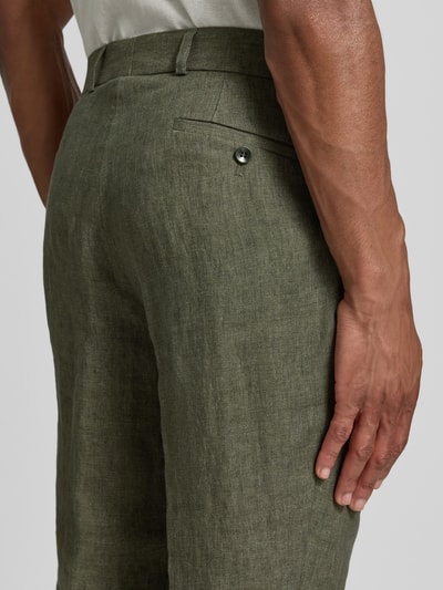 Männermodel trägt Slim Fit Leinenhose aus reinen Leinen Modell 'Tomte' von Carl Gross in Olivgrün mit Bügelfalten, Gesäßtaschen, Knopf- und Reißverschluss, Ganzkörperansicht Rückansicht. Bundweite bei Größe 50: 45 cm, Innenbeinlänge bei Größe 50: 84 cm.