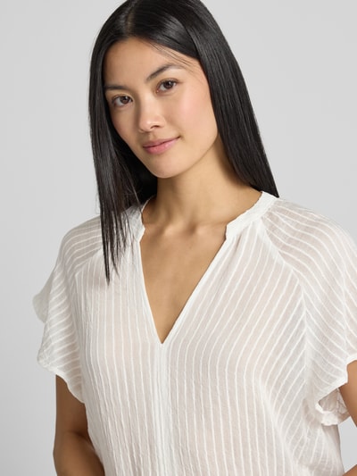 Vrouwenmodel draagt Blusenshirt aus Viskose-Mix mit Raglanärmeln van zero in witte kleur, structuurpatroon, serafinohals, loose fit, nahaufnahme bovenlichaam.