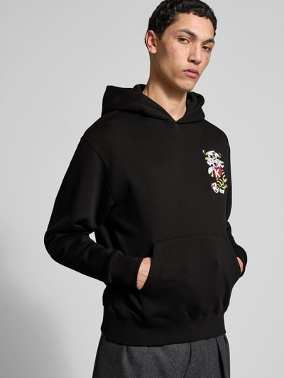 Männermodel trägt Oversized Hoodie aus reiner Baumwolle von Kenzo, schwarze Farbe, Label-Stitching, Känguru-Tasche, lockere Passform, elastische Abschlüsse, Rückenlänge bei Größe M 66 cm, Nahaufnahme Oberkörper.