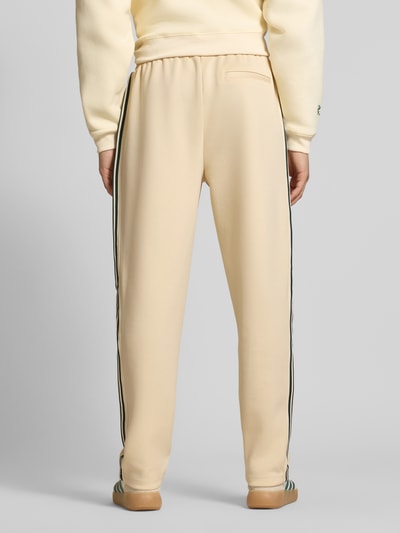 Männermodel trägt Regular Fit Sweatpants mit elastischem Bund Modell 'RIBER' von Only & Sons, cremefarben mit Kontraststreifen, feine Webstruktur, Ganzkörperansicht Rückansicht.