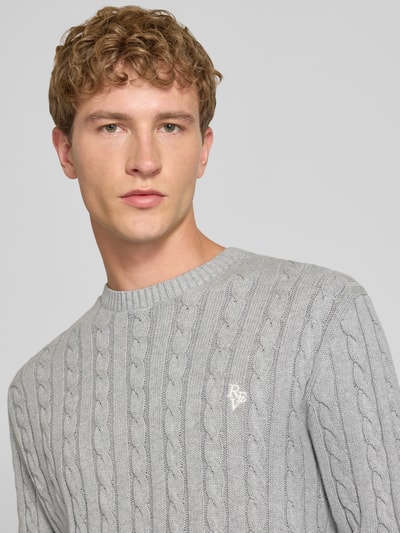 Männermodel trägt Slim Fit Strickpullover reine Baumwolle von REVIEW in Grau mit Zopfmuster und Logo Stickerei, Nahaufnahme Oberkörper.