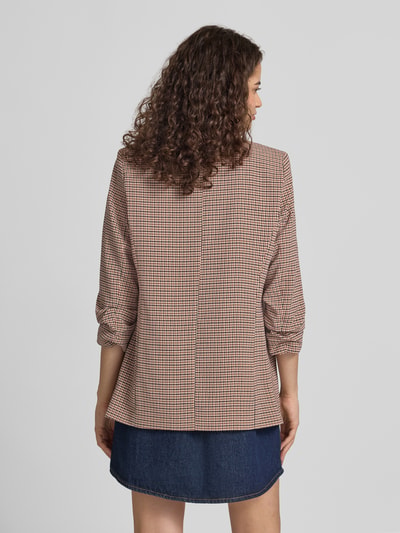 Frauenmodel trägt Shaped Fit Longblazer mit Schalkragen Modell 'BOSELLA' von PIECES in kleingemustertem Braun und Weiß, kombiniert mit Jeansrock, Ganzkörperansicht Rückansicht.