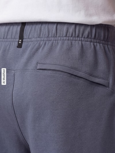 Männermodel trägt Loose Fit Sportshorts mit Baumwoll-Anteil von Under Armour, grau, glatte Struktur, Detailaufnahme Rückansicht, KI-modifiziertes Bild.