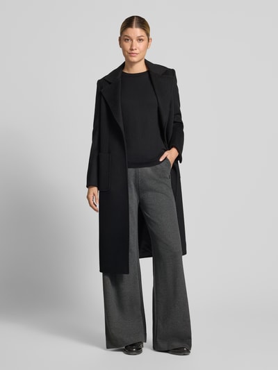 Vrouwenmodel draagt Wide Leg Hose mit elastischem Bund van ARMEDANGELS in grijs, zwart shirt en lange zwarte jas, Ganzkörperaanzicht van voren.