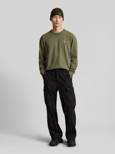 Männermodel trägt Relaxed Fit Langarmshirt aus reiner Baumwolle von Polo Ralph Lauren in Olivgrün, schwarze Cargo-Hose, Ganzkörperansicht von vorne. Herren Langarmshirt von Polo Ralph Lauren