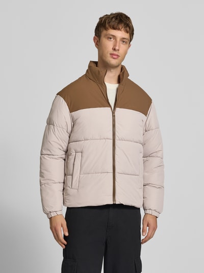 Männermodel trägt Steppjacke mit Stehkragen Modell 'RAZE' von JACK & JONES in Beige und Braun, Reißverschluss, Ganzkörperansicht von vorne.