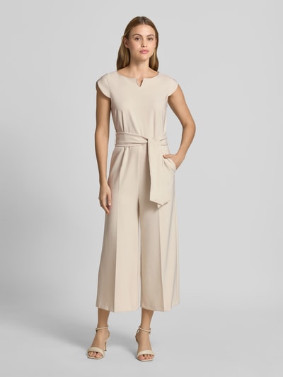 Modelka nosi Regular Fit Jumpsuit mit Bügelfalten od Betty Barclay z elastycznej mieszanki materiałów, odpinana materiałowa tasiemka, jednokolorowy, z krótkim rękawem, długość tyłu w rozmiarze 36: 133 cm, szerokość w rozmiarze 36: 47 cm, całkowita długość w rozmiarze 36: 40 cm, długość wewnętrzna nogawki w rozmiarze 36: 62 cm, jasny beż, kanty, prostokątne nogawki, gładka faktura, krój regular fit, całkowity widok z przodu