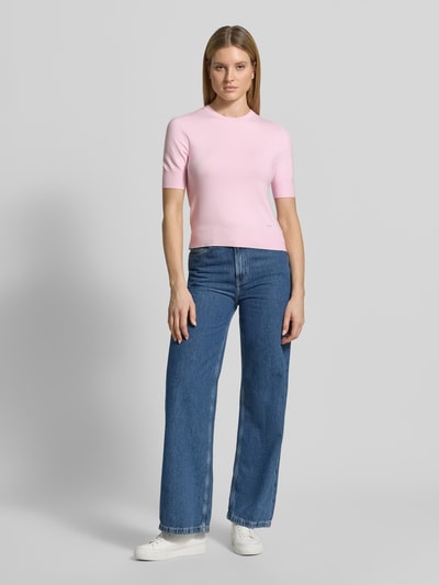 Kobiece modelka nosi Slim Fit T-Shirt aus Viskose-Mix od s.Oliver RED LABEL w jasnoróżowym kolorze, imitacja dzianiny, aplikacja z metką, okrągły dekolt, krótki rękaw, prążkowane wykończenie, drobny splot, mieszanka wiskozy; widok całej sylwetki od przodu.