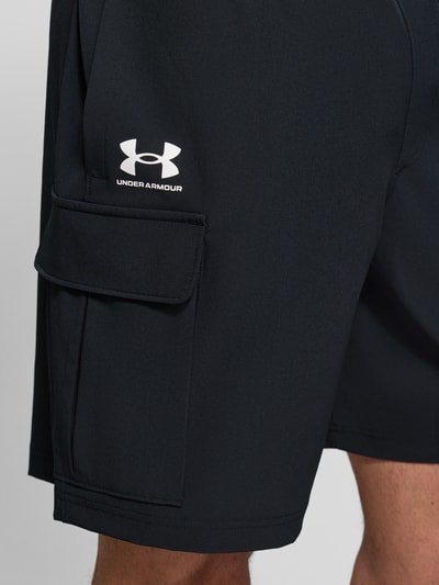 Männermodel trägt Straight Fit Shorts mit Cargo-Taschen Modell 'Vibe' von Under Armour in Schwarz mit Logo-Print, Nahaufnahme Oberschenkel.